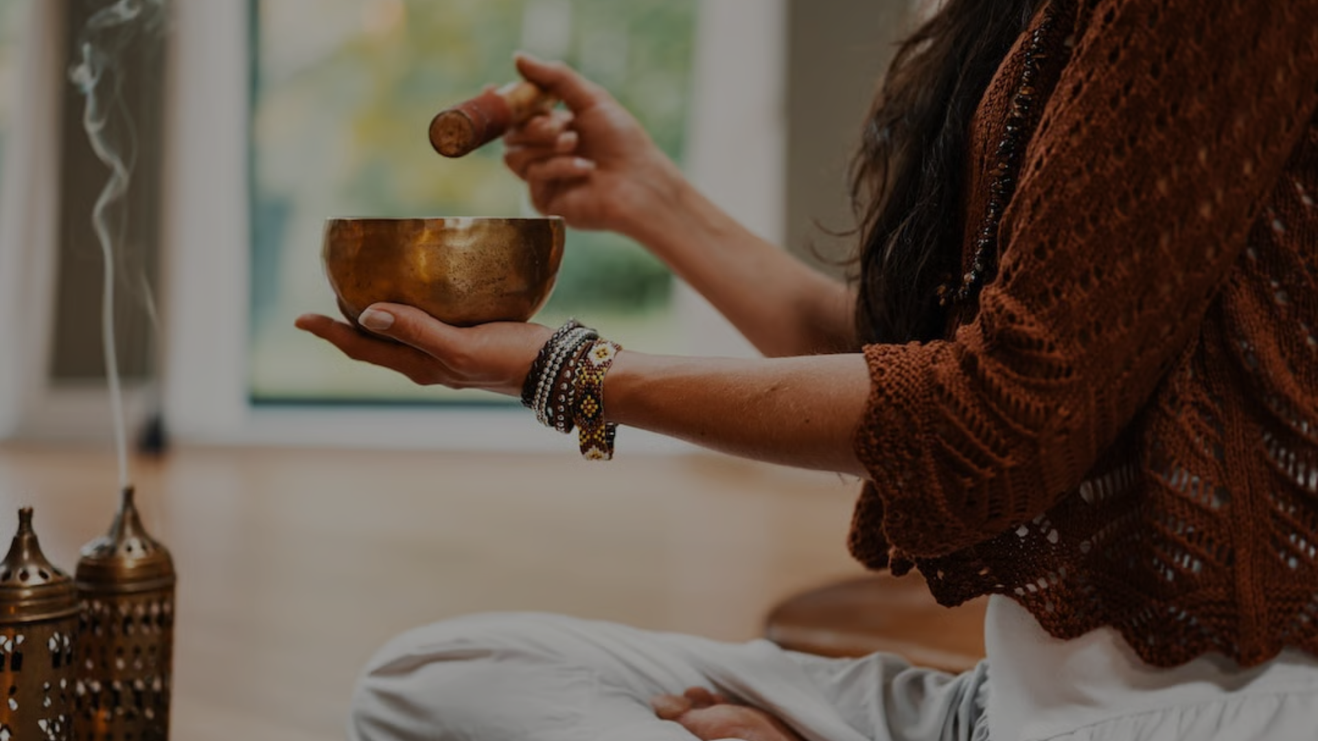 Person holding a singing bowl in a serene setting with incense
