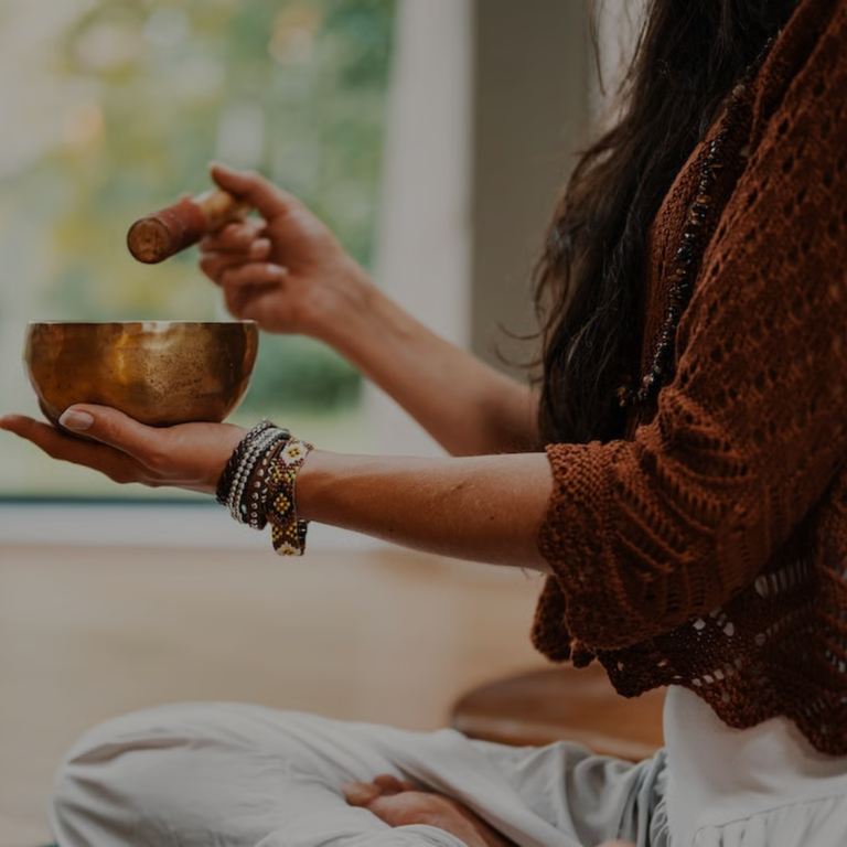 Person holding a singing bowl in a serene setting with incense