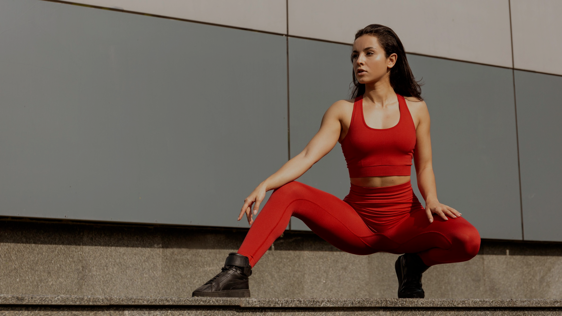 Woman in red athletic wear sitting on a concrete surface with a gray wall background