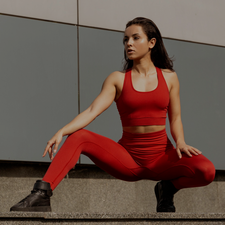 Woman in red athletic wear sitting on a concrete surface with a gray wall background